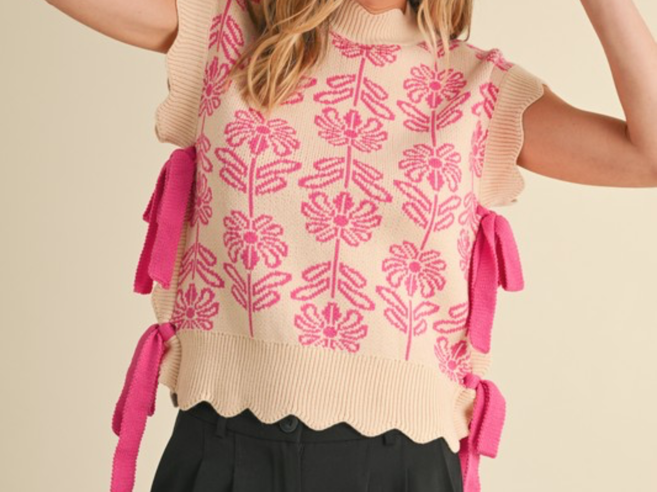 Woman wearing a ribbed scallop floral sweater vest with pink tassels on a beige background